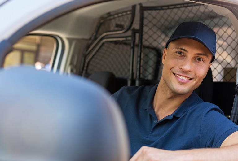 Mann in einfarbigem Shirt und Cap schaut freundlich aus einem offenen Autofenster