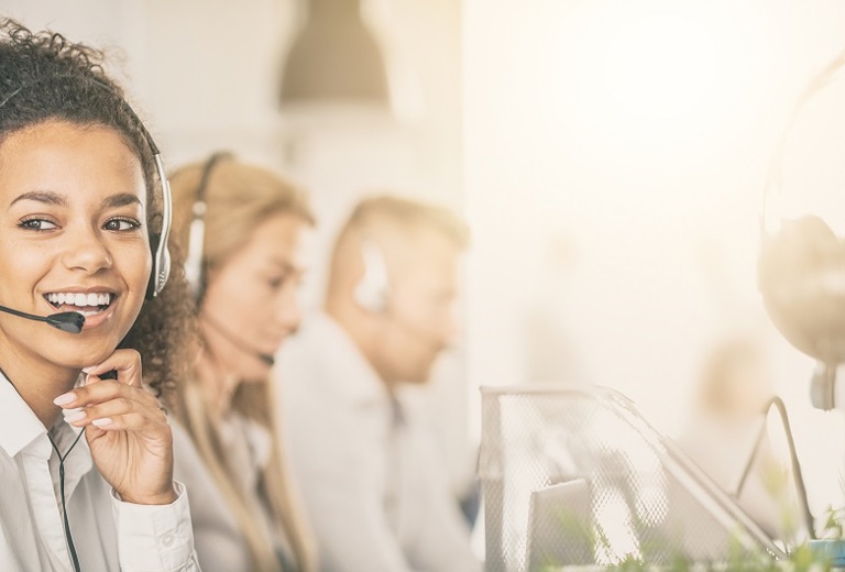 lächelnde Frau mit Headset neben weiteren telefonierenden Personen