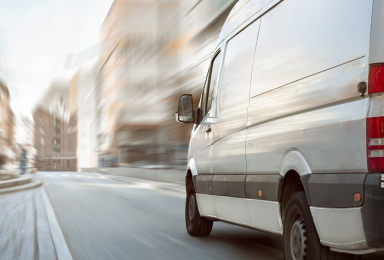 weißer Transporter fährt durch eine Straße in einer Stadt